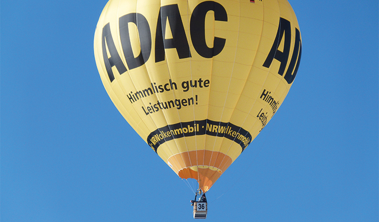 Gelber ADAC-Heißluftballon am Himmel mit Korb; Text: "Himmlisch gute Leistungen!"