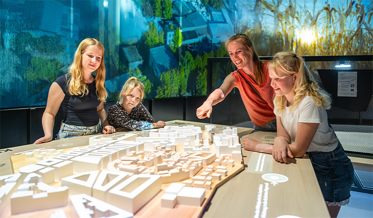 Vier blonde Personen betrachten mit Interesse ein beleuchtetes Architekturmodell